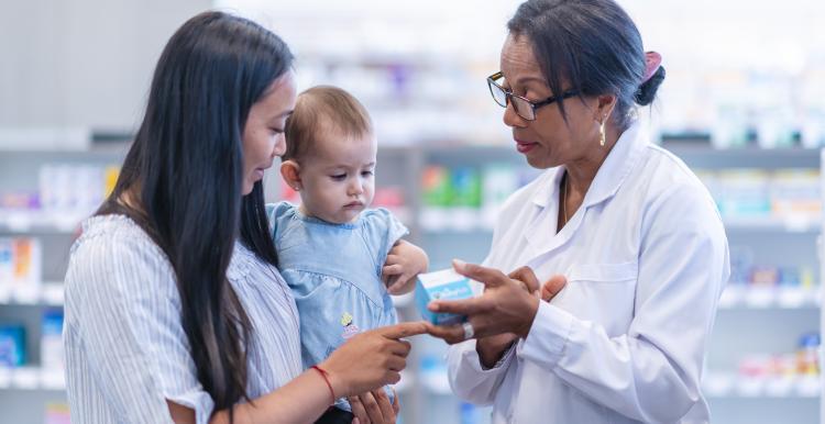 A woman and baby talking to a pharmacist in a pharmacy