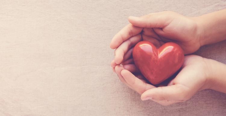 A pair hands holding a red heart shaped ornament