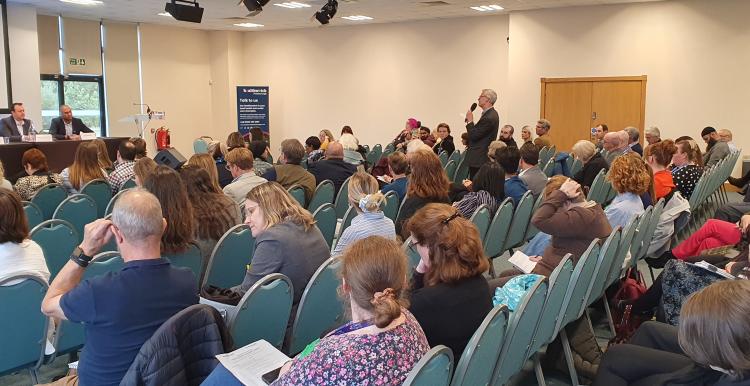 A member of the audience puts a question to a panel of experts at our Summit event. Audience members are watching.