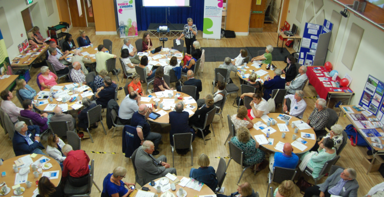 Picture shows room full of people sat at tables 