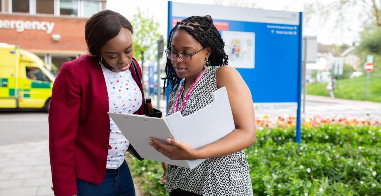 Two women standing outside a hospital looking at a document