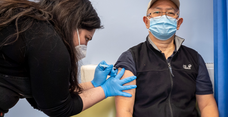 Man indoors wearing face covering receiving a Covid-19 vaccination from a health worker