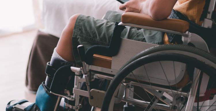 A young wheelchair user in a bedroom and holding a mobile phone