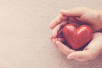 A pair hands holding a red heart shaped ornament