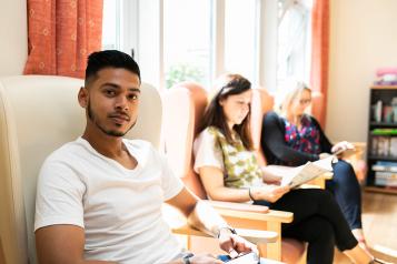 Three people sitting in a room. Two are reading and the other is looking at the camera.