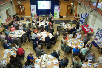 Picture shows room full of people sat at tables 